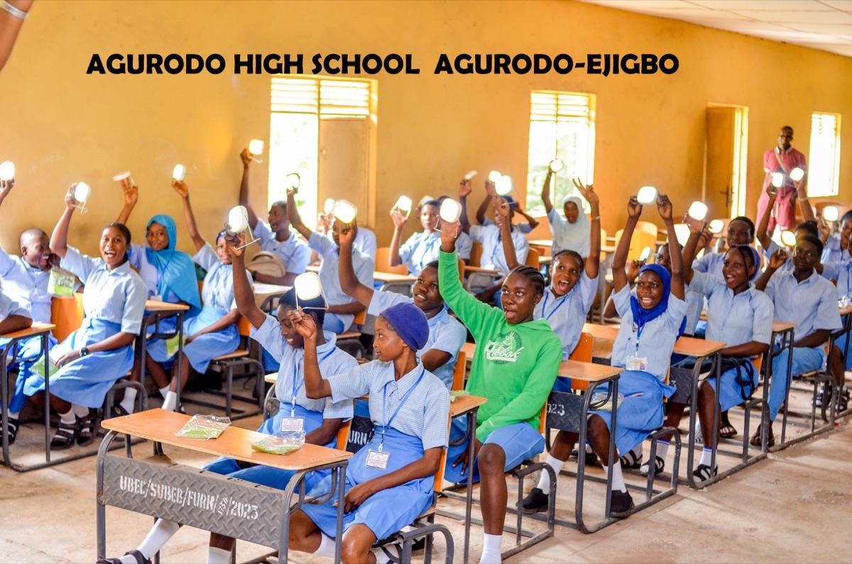 Joyful students at Agurodo High School raising lit solar lanterns high in the air after receiving them through the One Child One Lantern initiative