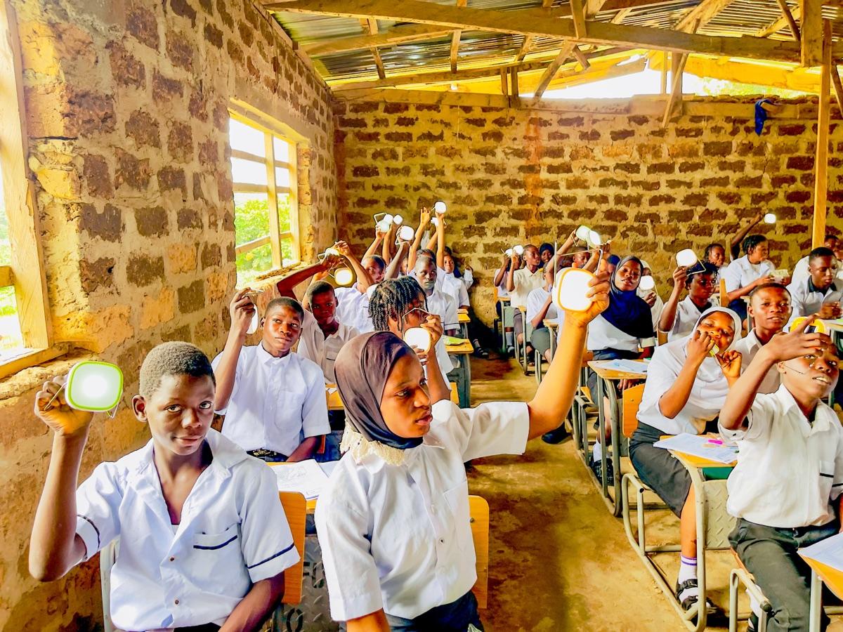 Rural school students in Osun State raising solar lanterns through open brick classroom walls, capturing the reach of the Imole Solar Lantern Campaign